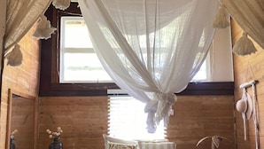 Une chambre à coucher avec un lit à baldaquin, des murs en bois, une fenêtre et une table de chevet sur laquelle se trouve un vase.