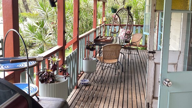 Une terrasse en bois avec une table et des chaises, entourée de plantes en pot et d’un barbecue.