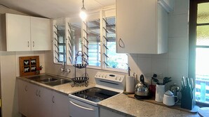 Une cuisine avec des armoires blanches, un évier en acier inoxydable, une cuisinière et une fenêtre donnant sur l’extérieur.