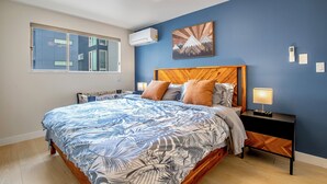 Ein Schlafzimmer mit einem großen Bett, einem Holz-Kopfteil, einem Nachttisch mit Lampe und einer Wand-Klimaanlage.