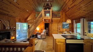 Un interior de cabaña acogedor con una escalera de madera, chimenea, comedor y cocina.