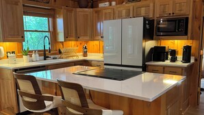 Una cocina moderna con armarios de madera, una isla central con taburetes de bar, un microondas integrado y una cafetera.