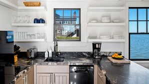 Cocina moderna con encimera negra, electrodomésticos de acero inoxidable y ventana con vista a un edificio y al agua.