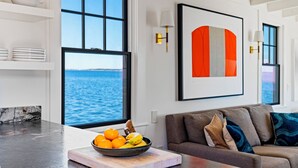 Una sala de estar moderna con vista al mar, un frutero en la encimera y un sofá con cojines.