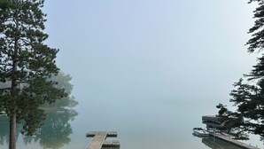 Une vue sur le lac avec un quai s’avançant dans l’eau, entouré d’arbres et d’une zone herbeuse aménagée avec des sièges extérieurs.