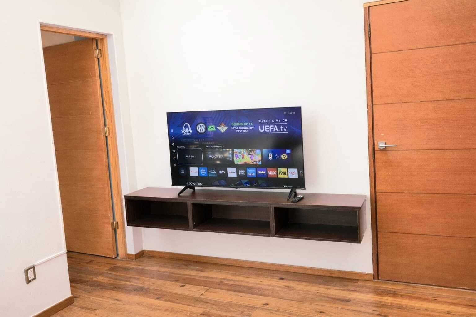Een televisie op een wandplank in een kamer met houten vloer en een deur.