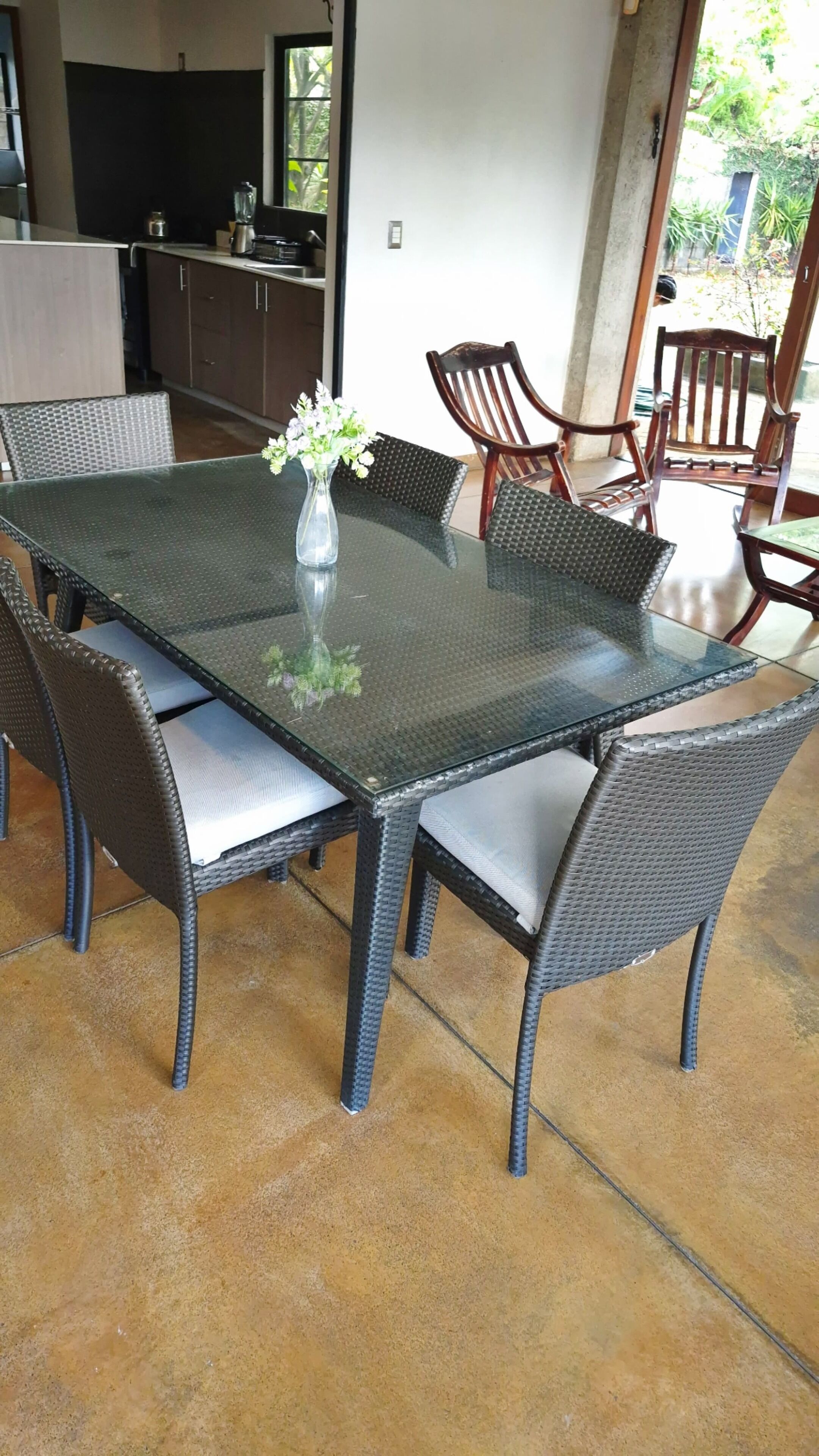 A dining table with wicker chairs, a vase with flowers, and a kitchen in the background.