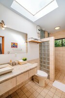 Un baño moderno con tragaluz, cabina de ducha, inodoro y tocador con lavabo y encimera.