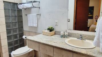 A modern bathroom with a large mirror, a sink, and a toilet. There is a towel rack with towels and a small plant on the countertop.