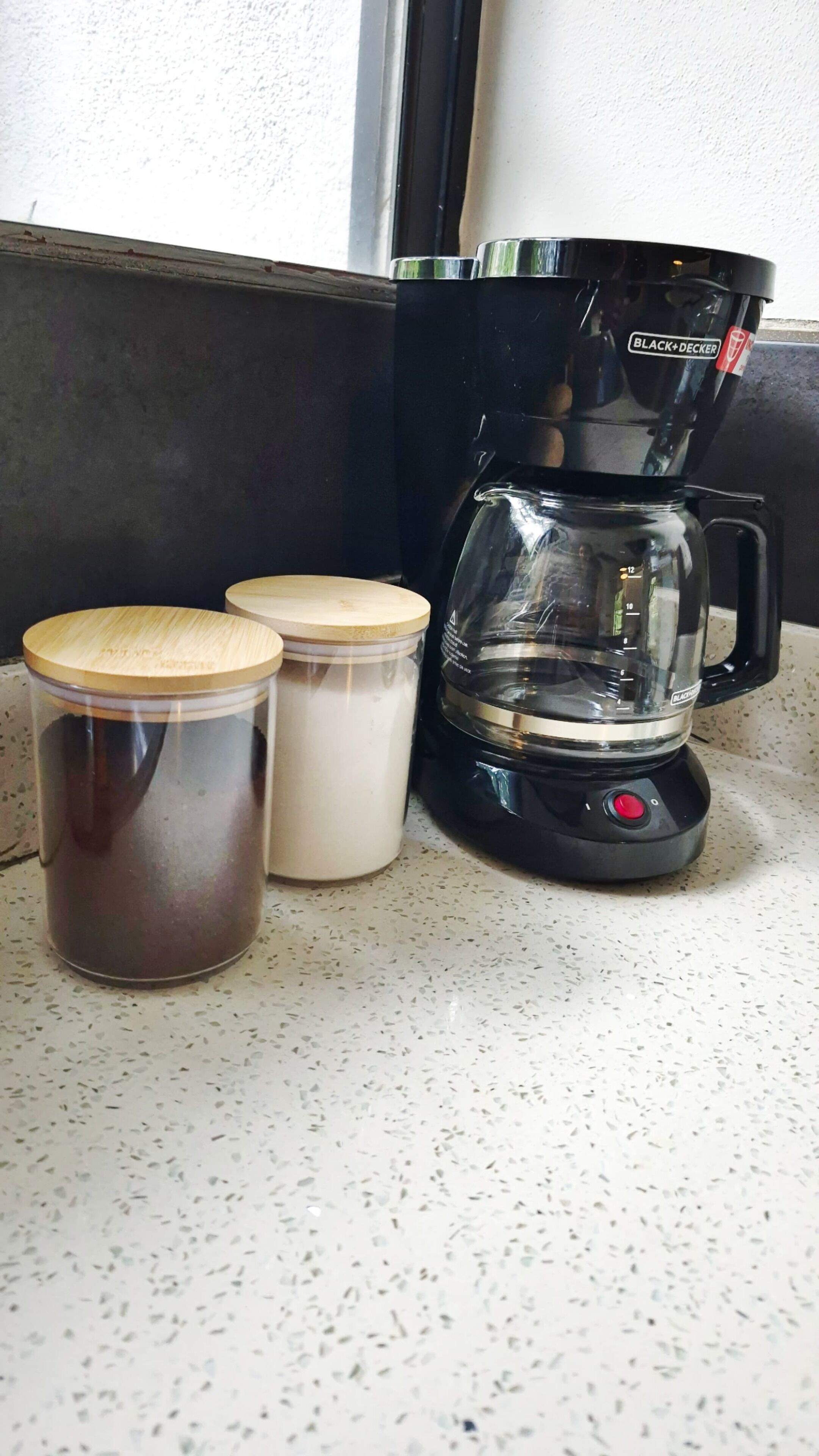 A coffee maker, two containers with lids, and a countertop.
