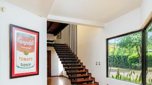 Een modern interieur met een gepolijste betonvloer, een houten trap, een groot raam met uitzicht op groen en een lijst met een afbeelding aan de muur.