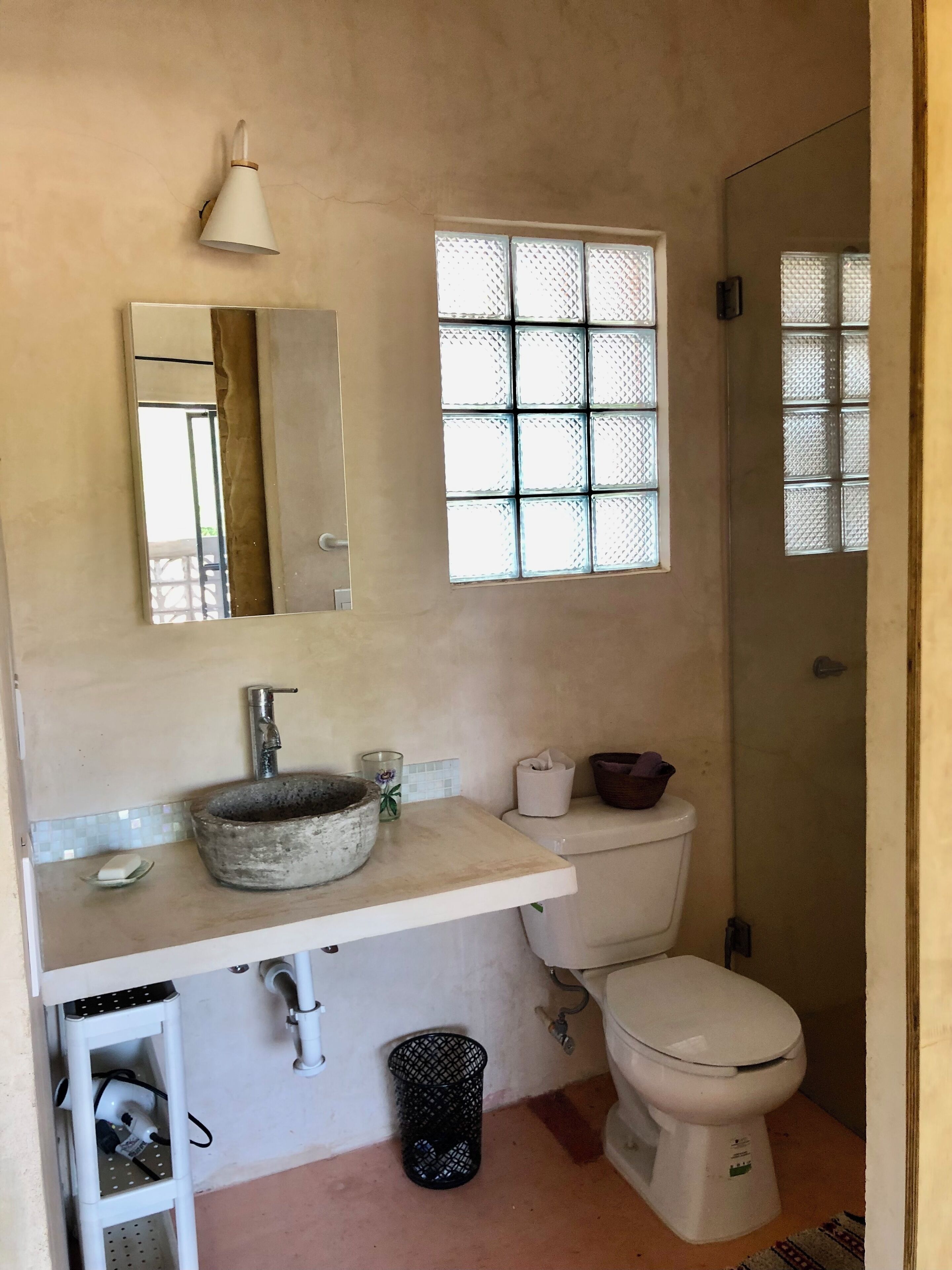 A bathroom with a sink, mirror, toilet, and window.