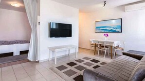 Ein modernes Wohnzimmer mit Flachbildfernseher an der Wand, einem Esstisch mit Stühlen, einer Bank und einem Sofa.