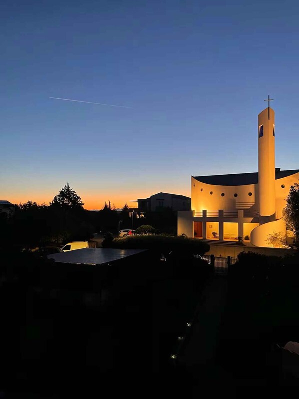 Ein modernes Gebäude mit einem markanten Turm und einer flachen Dachfläche, umgeben von Grünflächen und blauem Himmel.