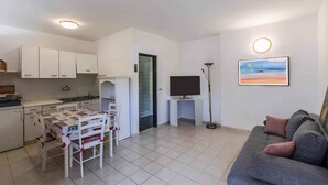 A modern living space with a kitchen, dining area, and a living room with a sofa and a painting. - Holiday apartment Flat with pool (Pješćana Uvala)