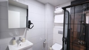 A modern bathroom with a glass shower enclosure, a white sink with toiletries, and a toilet. - Evra Suites (İstanbul)