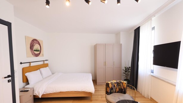 A modern hotel room with a bed, a small table, a chair, a wardrobe, and a TV. - Evra Suites (İstanbul)