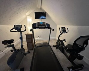 Een huisgym met een loopband, hometrainers en een televisiescherm.