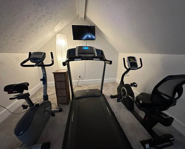 A home gym with a treadmill, stationary bikes, and a TV screen.