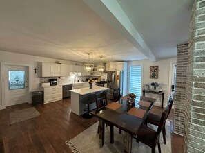 A spacious kitchen with a central island, dining area with a table and chairs, and a brick accent wall.