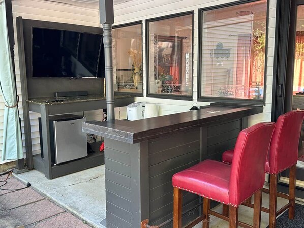 An outdoor kitchen area with a built-in grill, a refrigerator, and a bar counter with two red bar stools. - Historic Mattsville in Carmel (Carmel)