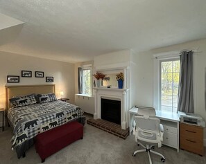 A bedroom with a bed, a desk, a chair, a fireplace, and a window.
