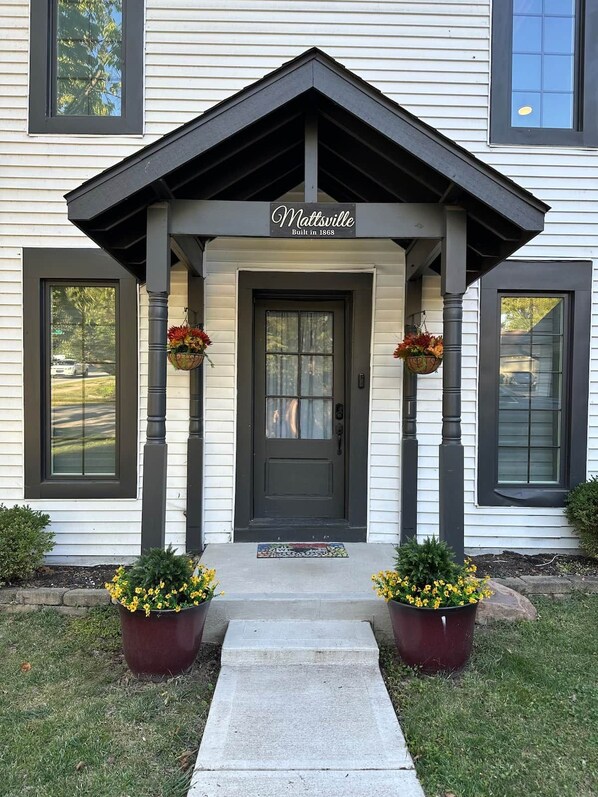 A two-story house with a front porch, a black front door, and a sign above the door that reads 'Mattsville Built in 1868.'