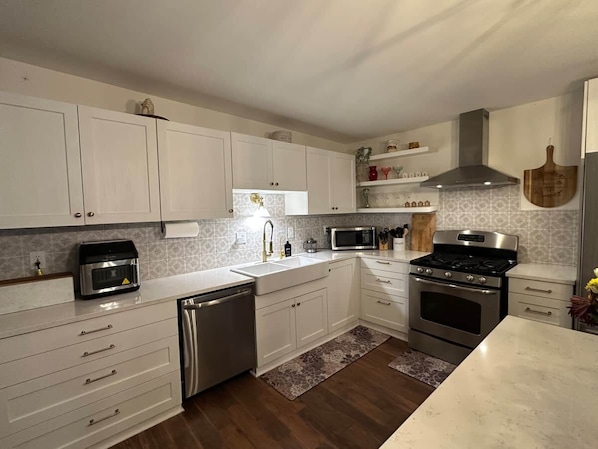 Een moderne keuken met witte kasten, roestvrijstalen apparatuur en een houtkachel.