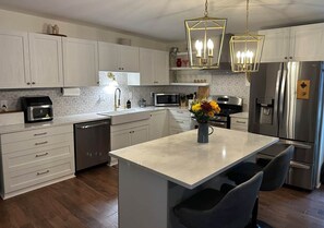 A modern kitchen with white cabinetry, stainless steel appliances, a central island with seating, and pendant lighting. - Historic Mattsville in Carmel (Carmel)