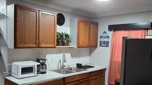 A compact kitchen with wooden cabinets, a white countertop, a microwave, a coffee maker, and a sink.