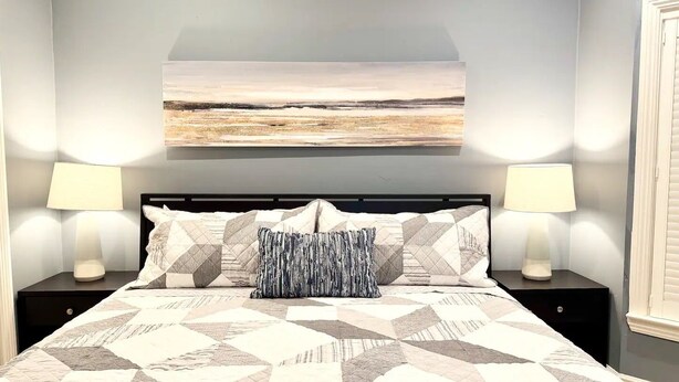 Ein Schlafzimmer mit einem Bett, zwei Nachttischlampen, einem Nachttisch und einem Wandbild.