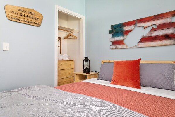 Un dormitorio con cama, cómoda, mesita de noche, lámpara colgante y una obra de arte en la pared.
