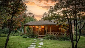 Eine Holzhütte mit einer Veranda, umgeben von einem Garten und Bäumen.