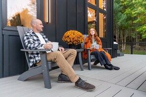 Two people sitting on outdoor benches with a large flower arrangement between them, on a wooden deck with a building in the background. - Finger Lakes Luxury Couples Retreat with Sauna, Hot tub and Cold Plunge (Alpine)