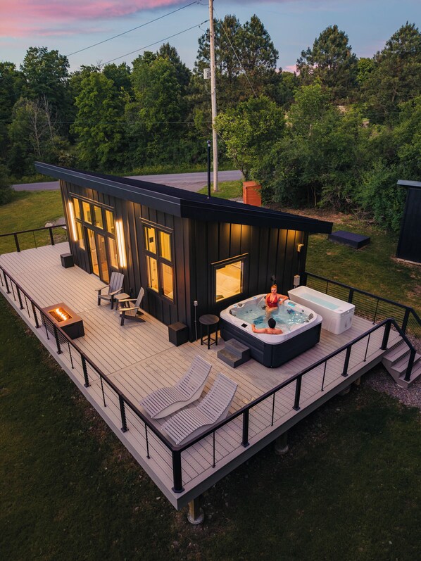 A modern outdoor deck with a hot tub, lounge chairs, and a fire feature. - Finger Lakes Luxury Couples Retreat with Sauna, Hot tub and Cold Plunge (Alpine)