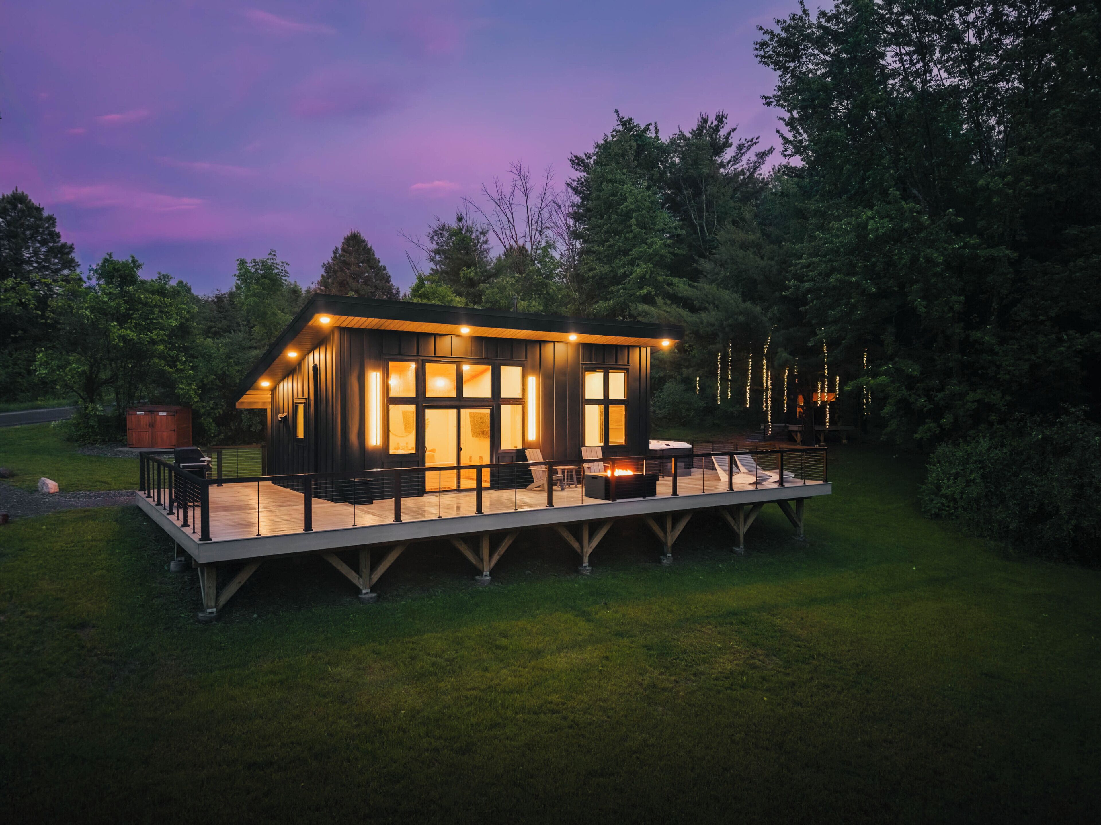 A modern cabin with a deck, large windows, and outdoor seating.