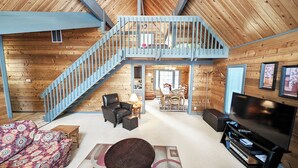 A spacious living area with a wooden interior, a staircase, a dining area, and a television. - Lava Top 1 - Updated Cabin, SHARC, Pet Friendly, Walk to SHARC (Sunriver)