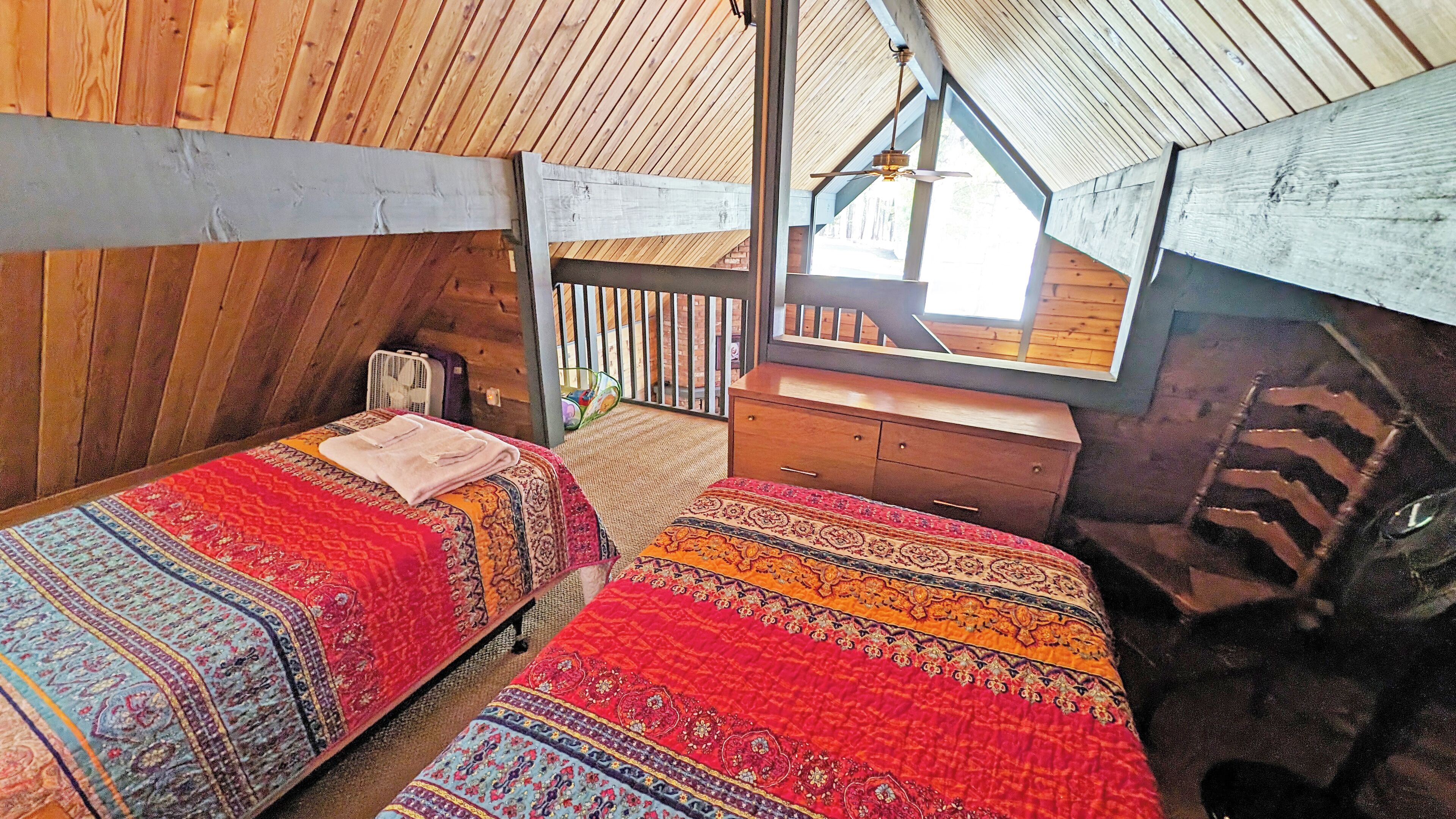 A cozy attic bedroom with two beds, a wooden ceiling, and a small desk.