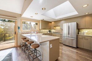 A modern kitchen with a central island, bar stools, a large refrigerator, and a view of the outdoors. - Lone Eagle Landing 2 - Updated, A/C, Hot Tub, SHARC Passes (Sunriver)