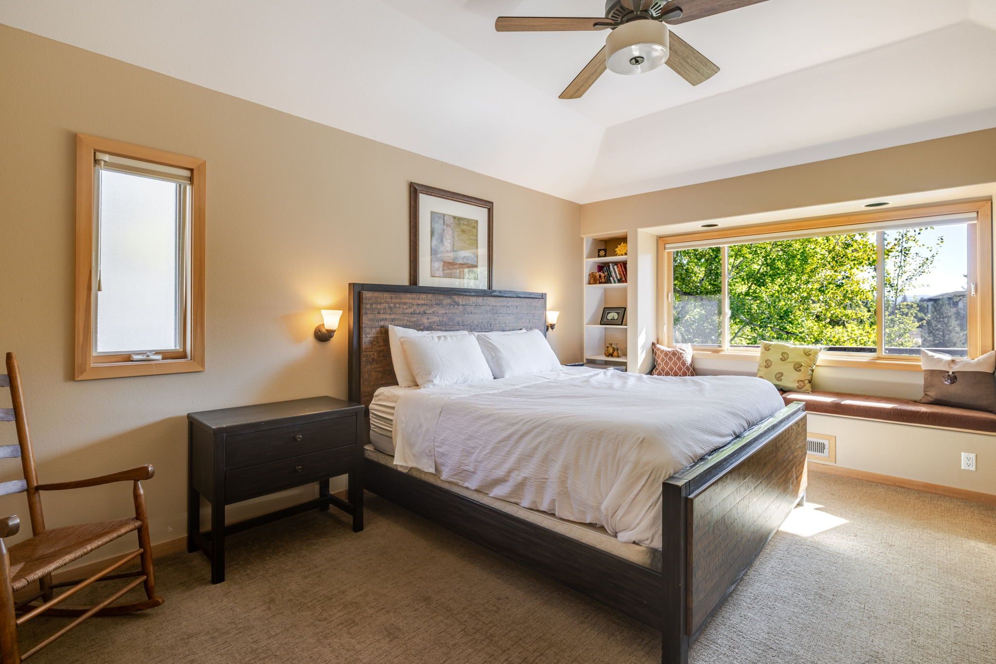 A bedroom with a bed, nightstand, chair, window, and ceiling fan.