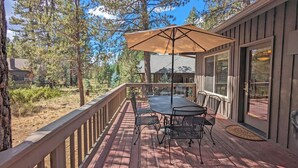 A wooden deck with a table and chairs, an umbrella, and a view of a forested area.