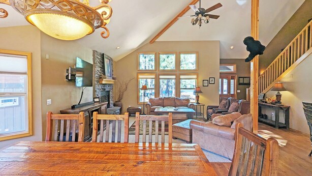 A spacious living area with a wooden floor, a stone fireplace, a large window with a view of trees, and a ceiling fan.