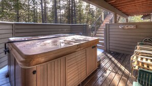 Ein hölzernes Whirlpool auf einer Holzterrasse mit überdachtem Bereich, umgeben von Bäumen.