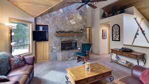 Ein gemütliches Wohnzimmer mit Kamin aus Stein, Holzbalkendecke und Fernseher auf einem Regal.