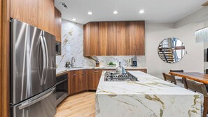 A modern kitchen with wooden cabinets, a stainless steel refrigerator, a marble countertop island, and a built-in stove. - Walk to Slopes Hot Tub + Balcony + Views Mins to Main Street Deer Valley Haven by Avantstay (Park City)