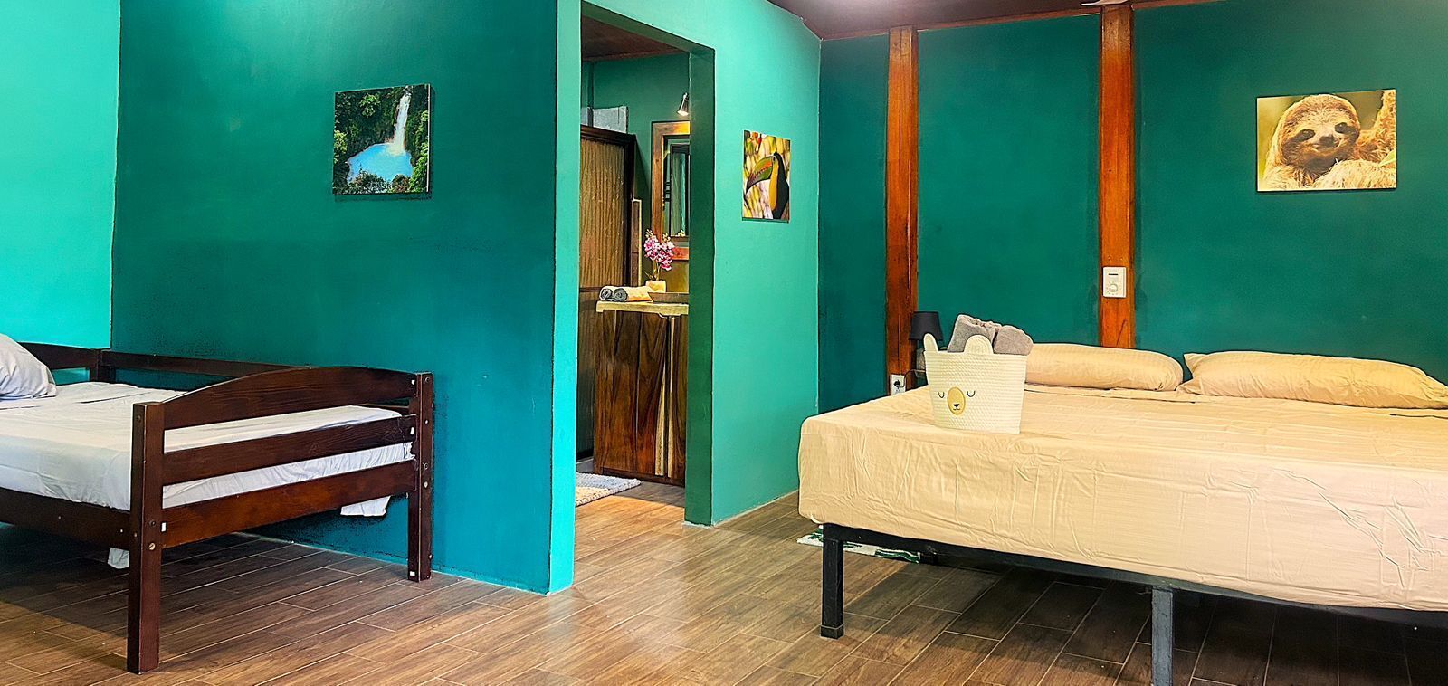 Ein Zimmer mit einem hölzernen Bett, einem zusätzlichen Bett, türkisblauen Wänden und einem Holzboden.