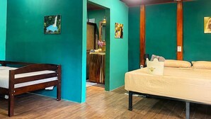 A room with a wooden bed, a smaller bed, teal walls, and a wooden floor. - Blue java banana (Tamarindo)