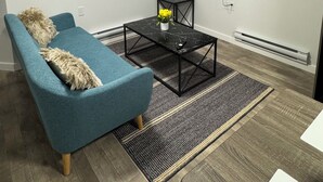 A modern living room with a sofa, a coffee table, a TV, and a small table with a book. - 1 BHK private basement suite (Regina)