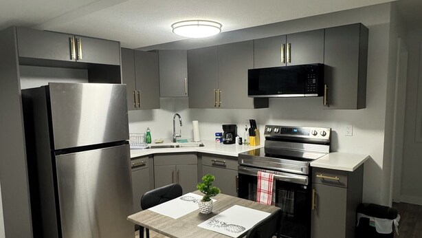 A modern kitchen with stainless steel appliances, a dining area with a table and chairs, and a microwave above the counter. - 1 BHK private basement suite (Regina)