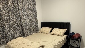 A bedroom with a bed, curtains, a nightstand, and a wooden floor. - 1 BHK private basement suite (Regina)